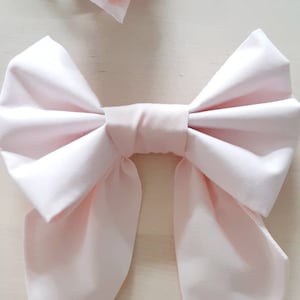 May include: A large, pale pink satin bow with long tails. The bow is tied in a classic style with a centre knot.