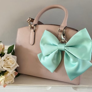May include: A light pink handbag with a light blue satin bow attached to the handle.