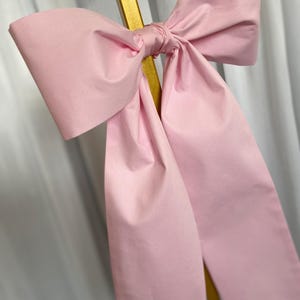 以下が含まれることがあります： 金色の棒に結ばれた大きなピンクのリボン。リボンは柔らかく絹のような生地で作られています。