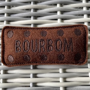 May include: Brown felt pillow with the word "BOURBON" embroidered in white. The pillow has a dotted pattern.