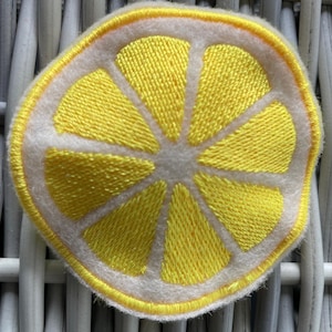 May include: A yellow embroidered lemon slice patch with a white background. The patch is perfect for adding a touch of summer to your clothing or accessories.