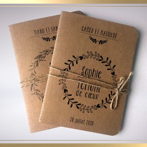 May include: Two brown kraft paper notebooks tied together with twine. The top notebook has the text "Samer et Mathilde" and "Sophie" in a wreath design. The bottom notebook has the text "Manu et Fan". Both notebooks have the text "T&eacute;moin de c&oelig;ur" and "26 Juillet 2020".