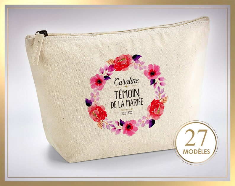 May include: A beige canvas cosmetic bag with a black zipper. The bag features a floral wreath design in pink and purple hues, with the text "Caroline T&Eacute;MOIN DE LA MARI&Eacute;E 10.09.2022". A circular emblem displays the number "27" and the word "MOD&Egrave;LES".