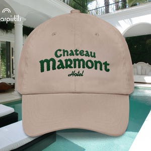 Może przedstawiać: Beżowa czapka z daszkiem z zielonym haftem z napisem "Chateau Marmont Hotel".