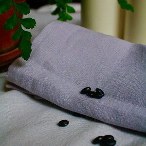 May include: Black beans scattered on a white linen tablecloth with a folded purple linen napkin on top.