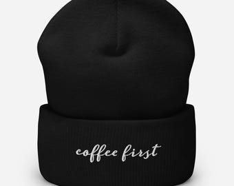 May include: Black beanie with the embroidered phrase "coffee first" in white script. The beanie is a soft, knitted hat, perfect for cold weather. The hat is a versatile accessory for any casual outfit.