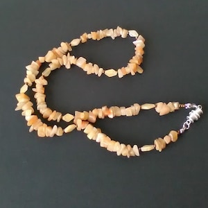 Peut inclure: Un long collier composé de petites pierres irrégulières de couleur brun clair. Le collier a un fermoir argenté.