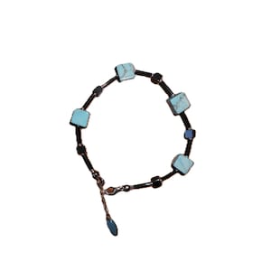 May include: A black bracelet with turquoise square beads. The bracelet has a silver clasp.