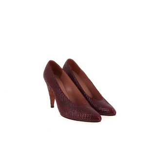 Puede incluir: Un par de zapatos de salón de color burdeos con estampado de piel de serpiente, punta puntiaguda y tacón de aguja.