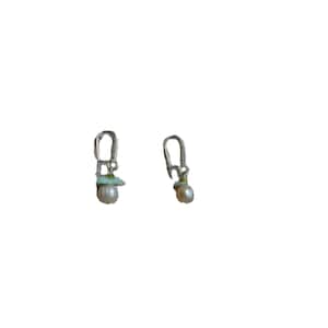 Peut inclure: Une paire de boucles d'oreilles en argent avec une petite perle et un charme vert et blanc suspendu à chaque boucle.