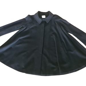 Peut inclure: Un manteau noir avec une conception de jupe évasée. Le manteau présente un col classique, des manches longues et un devant boutonné. Le manteau a deux poches et est fait d'un tissu lisse et sombre.