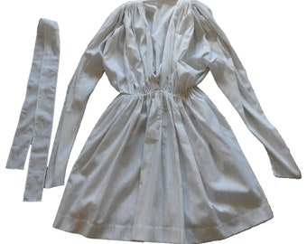 May include: A light gray dress with long sleeves and a V-neck. The dress has a gathered waist and a matching tie belt. The fabric appears to be a lightweight cotton or linen, suitable for warmer weather.