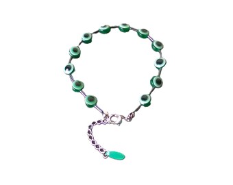 May include: A green evil eye bracelet with a silver chain and a green charm. The bracelet is made of small round beads with a white center and a green outer ring.