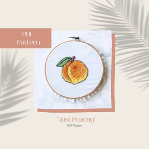 May include: Embroidered peach design in a wooden hoop. The peach is in shades of orange and yellow with a green leaf. The text "PDF Pattern" and "Just Peachy" are also visible.