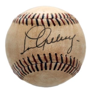 Op de afbeelding: Een vintage honkbal gesigneerd door Lou Gehrig, een beroemde honkbalspeler. De bal is wit met rode stiksels en een bruine lederen textuur.