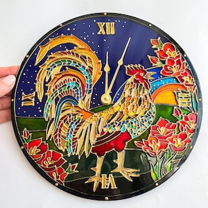 May include: A round clock with a stained glass design featuring a colourful rooster with a red comb and wattles. The rooster is surrounded by flowers and a starry night sky. The clock face has Roman numerals and gold hands.