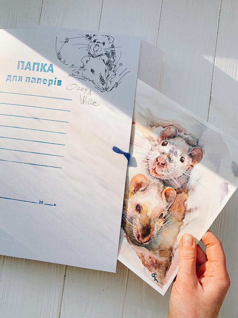 May include: A white paper folder with blue text and a sketch of two rats, labeled "Ozzy & Willie." A watercolor painting of two rats is held in front of the folder. The painting has a watercolor effect with shades of brown and white.