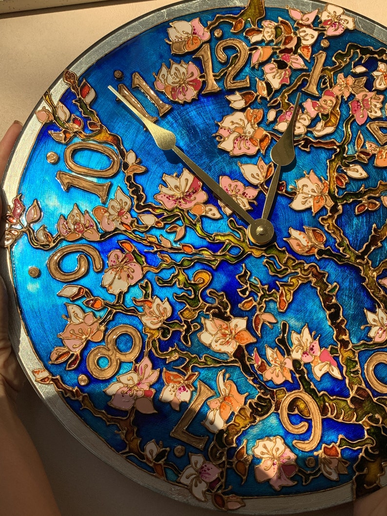 May include: A blue and gold clock with a floral design. The clock face features Roman numerals and gold hands. The floral design is painted in shades of pink, white, and green.