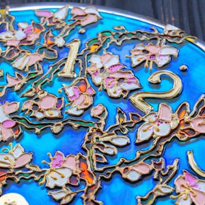 May include: Close-up of a blue clock face with gold numbers and a floral design. The flowers are painted in shades of pink, white, and gold.