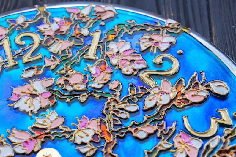 May include: Close-up of a blue clock face with gold numbers and a floral design. The flowers are painted in shades of pink, white, and gold.
