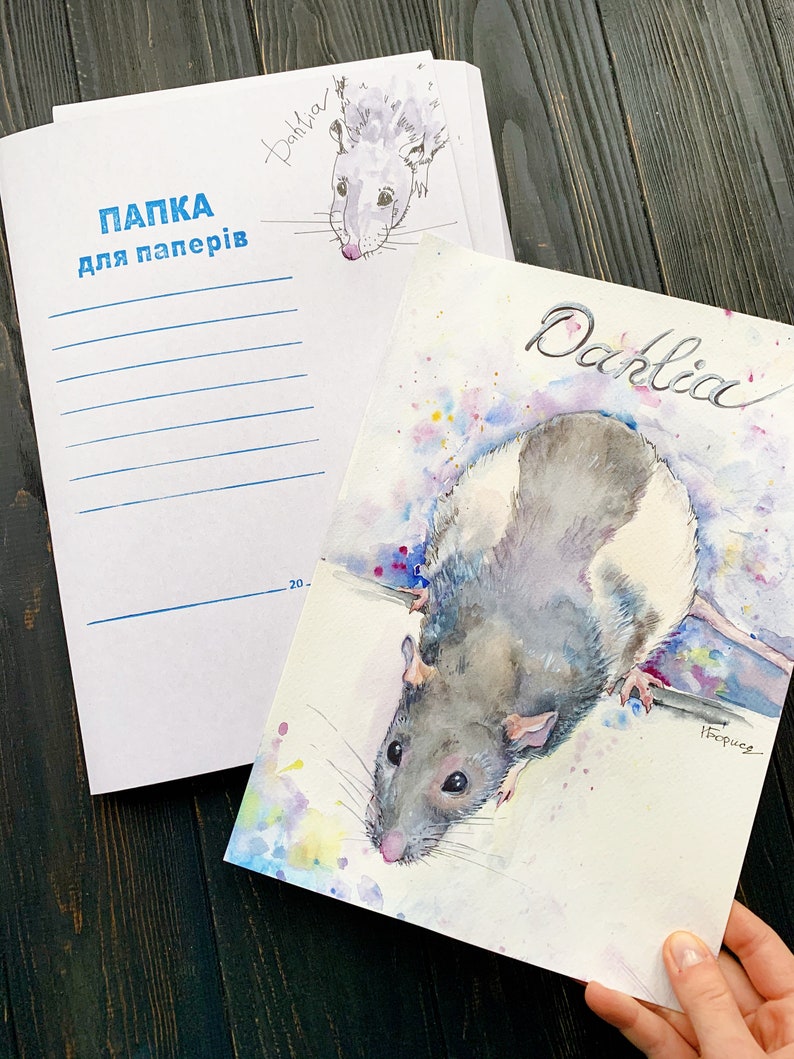 May include: Watercolor painting of a rat named Dahlia, with gray and white fur, and a pink nose. The painting is on a white paper, with colorful paint splatters. A matching notebook with the name "Dahlia" and the text "ПАПКА для паперів" is also visible.