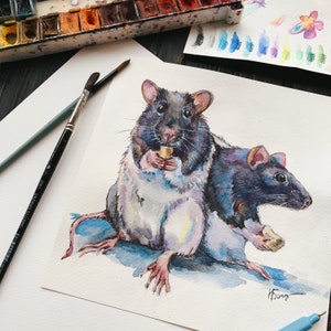 May include: Watercolor painting of two rats, one holding a small piece of food. The rats are black, white, and gray, with pink ears and feet. The artwork is on white paper, with paintbrushes and a watercolor palette in the background.