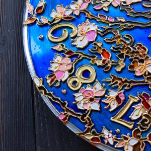 May include: A blue circular clock face with gold Roman numerals and a floral design. The flowers are painted in shades of pink, white, and gold.