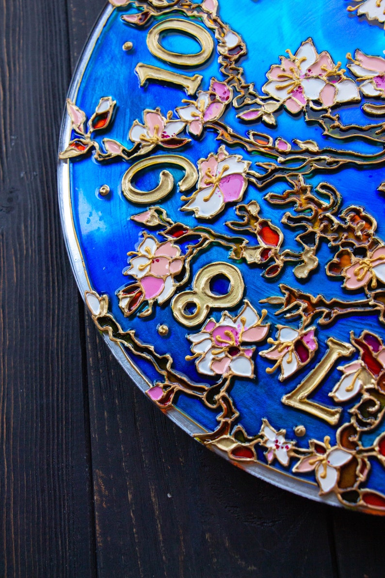 May include: A blue circular clock face with gold Roman numerals and a floral design. The flowers are painted in shades of pink, white, and gold.