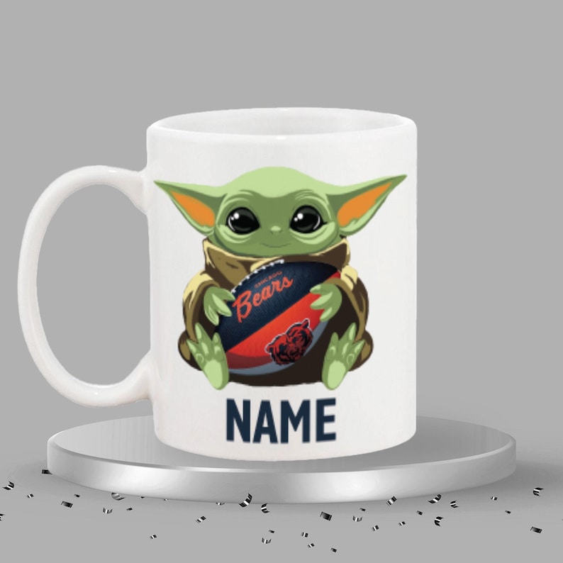 May include: White ceramic mug featuring a green cartoon character holding a football with the text "Bears". The mug also has the text "NAME" in navy blue. The character has large black eyes and pointed ears.