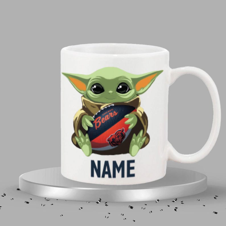 May include: White ceramic mug featuring a green alien character holding a football with the Chicago Bears logo. The mug has the word "NAME" printed in navy blue at the bottom.