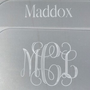Op de afbeelding: Een zilveren plaquette met de naam "Maddox" gegraveerd bovenaan en een monogram van de letters "MGL" gegraveerd in een schrijflettertype eronder.