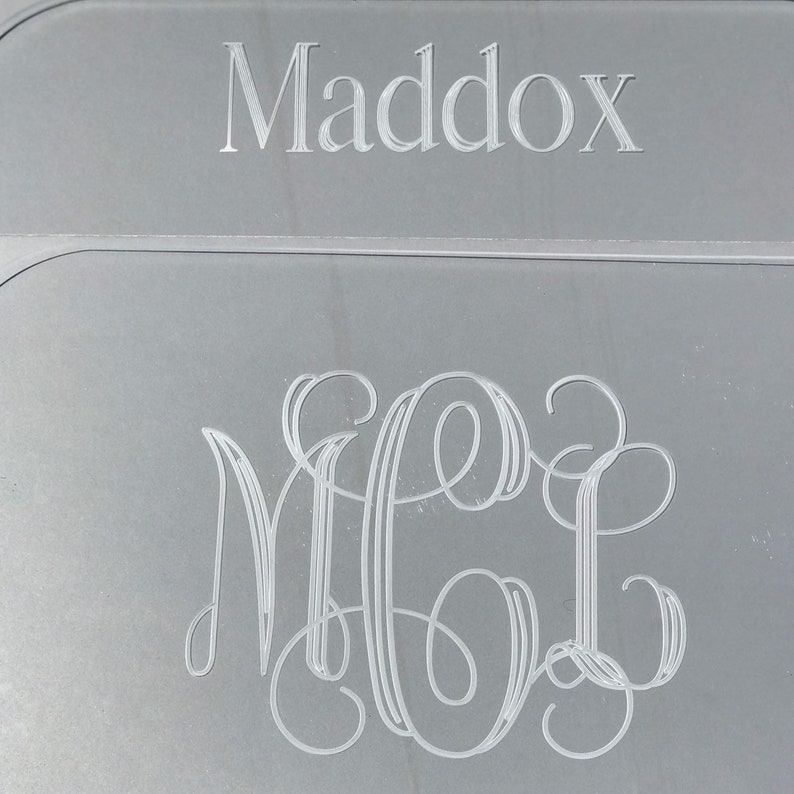 Op de afbeelding: Een zilveren plaquette met de naam "Maddox" gegraveerd bovenaan en een monogram van de letters "MGL" gegraveerd in een schrijflettertype eronder.