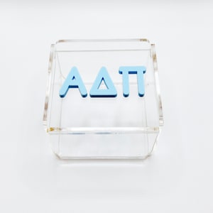 Pu&ograve; includere: Una scatola in acrilico trasparente con le lettere "AAT" in azzurro all'interno.