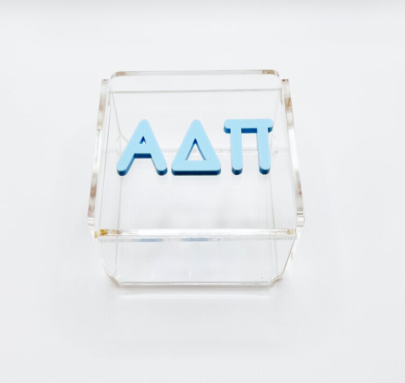 Pu&ograve; includere: Una scatola in acrilico trasparente con le lettere "AAT" in azzurro all'interno.