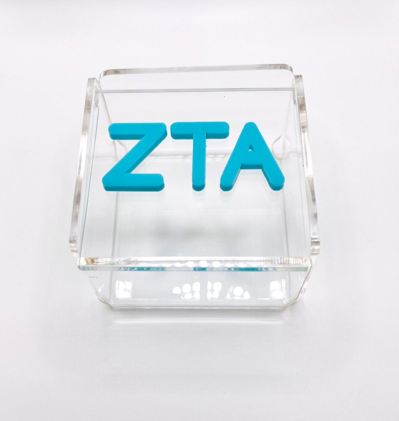 Pu&ograve; includere: Una scatola in acrilico trasparente con le lettere "ZTA" in blu.