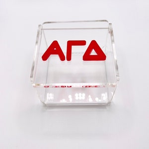Pu&ograve; includere: Una scatola in acrilico trasparente con le lettere "AFD" in rosso.