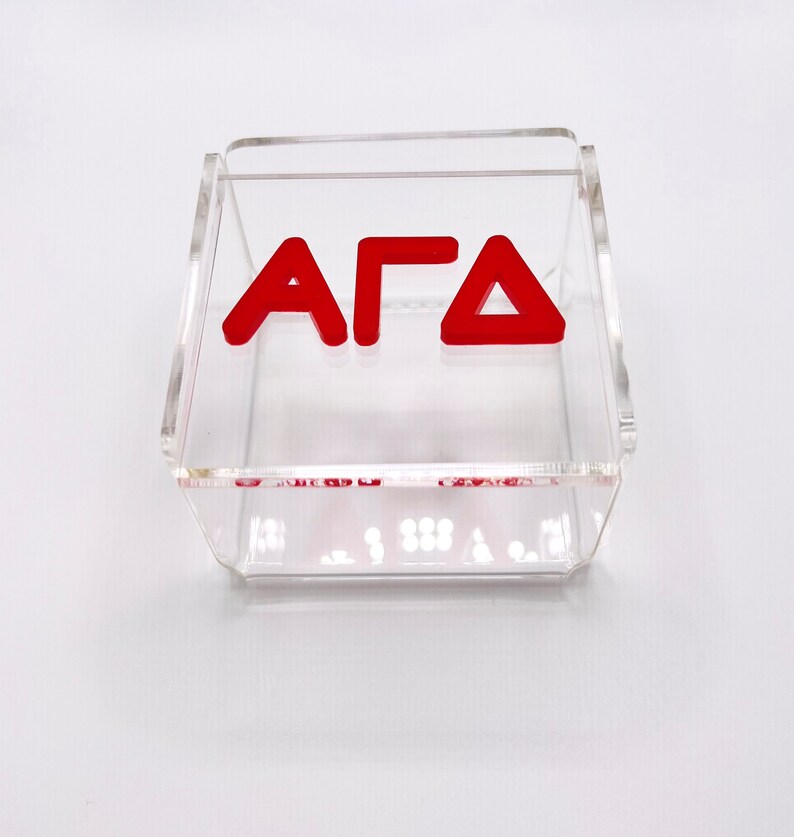 Pu&ograve; includere: Una scatola in acrilico trasparente con le lettere "AFD" in rosso.