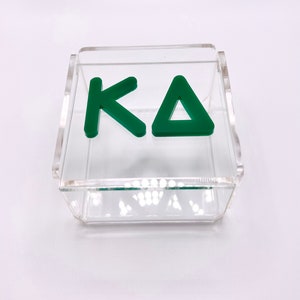 Pu&ograve; includere: Una scatola in acrilico trasparente con un logo "KA" verde all'interno. La scatola &egrave; perfetta per riporre piccoli oggetti o esporre cianfrusaglie.