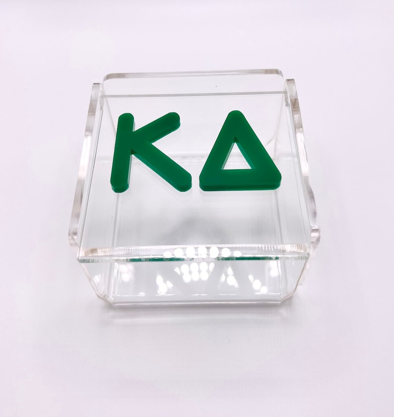 Pu&ograve; includere: Una scatola in acrilico trasparente con un logo "KA" verde all'interno. La scatola &egrave; perfetta per riporre piccoli oggetti o esporre cianfrusaglie.