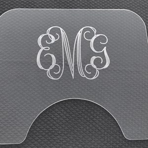 May include: A clear acrylic sign with a monogram of the letter "M" in a decorative script font.