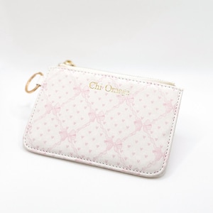 May include: A white zippered pouch with a pink and white heart and bow pattern. The pouch has a gold zipper and the text "Chi Omega" is printed in gold on the front.