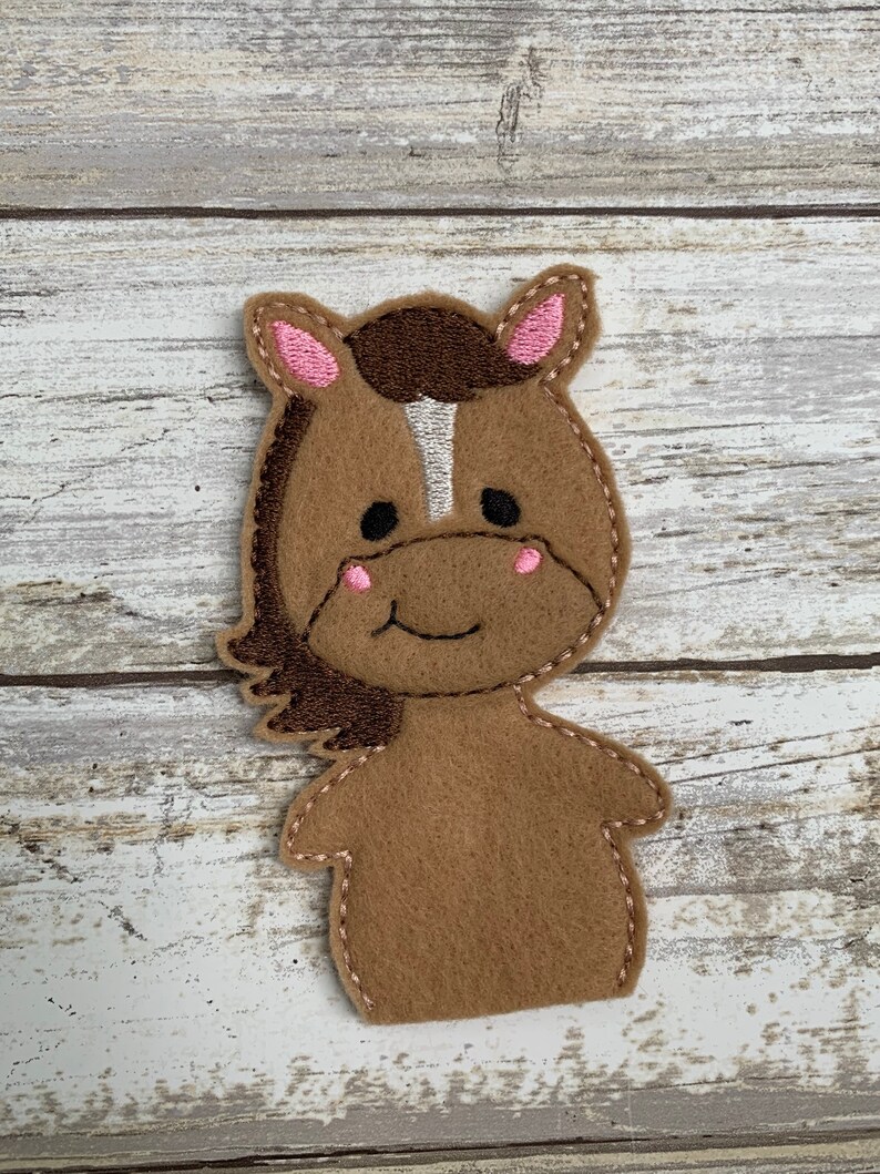 May include: Brown felt finger puppet of a horse with a white stripe down its face, pink ears, and a stitched smile.