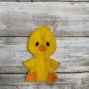 May include: A yellow felt chick finger puppet with black eyes, an orange beak, and orange feet.
