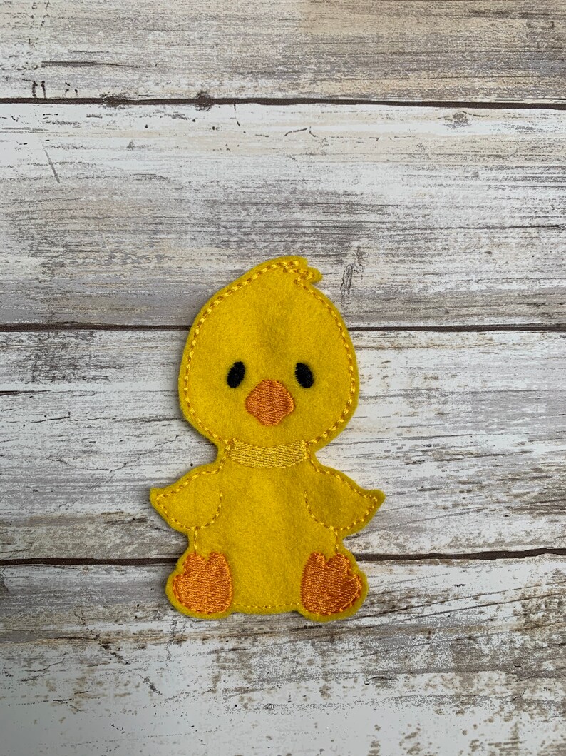 May include: A yellow felt chick finger puppet with black eyes, an orange beak, and orange feet.