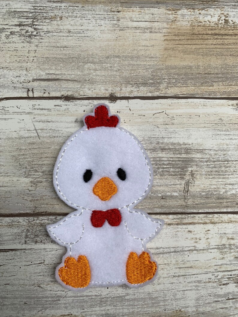 May include: White felt applique of a chick with red comb, orange beak, and feet, and a red bow tie.