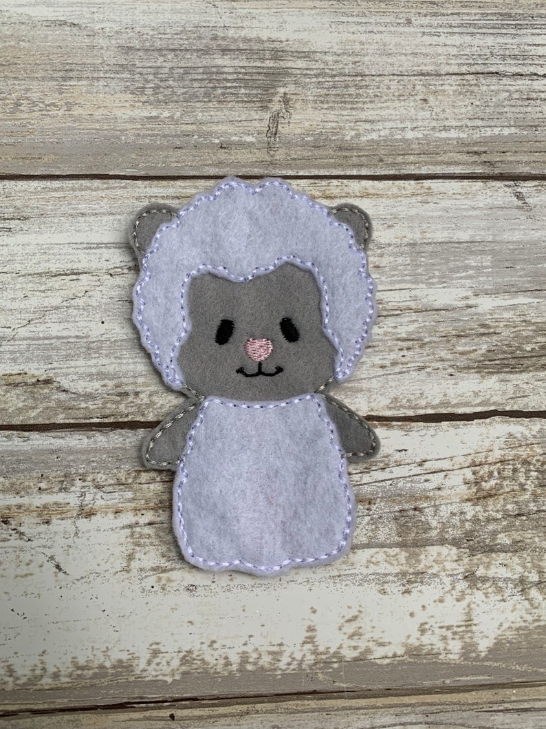 May include: A gray felt finger puppet shaped like a sheep with a white fluffy body and a pink nose.
