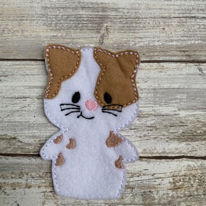May include: White felt finger puppet with brown felt ears and spots. The puppet has embroidered black eyes, a pink nose, and a smiling mouth.
