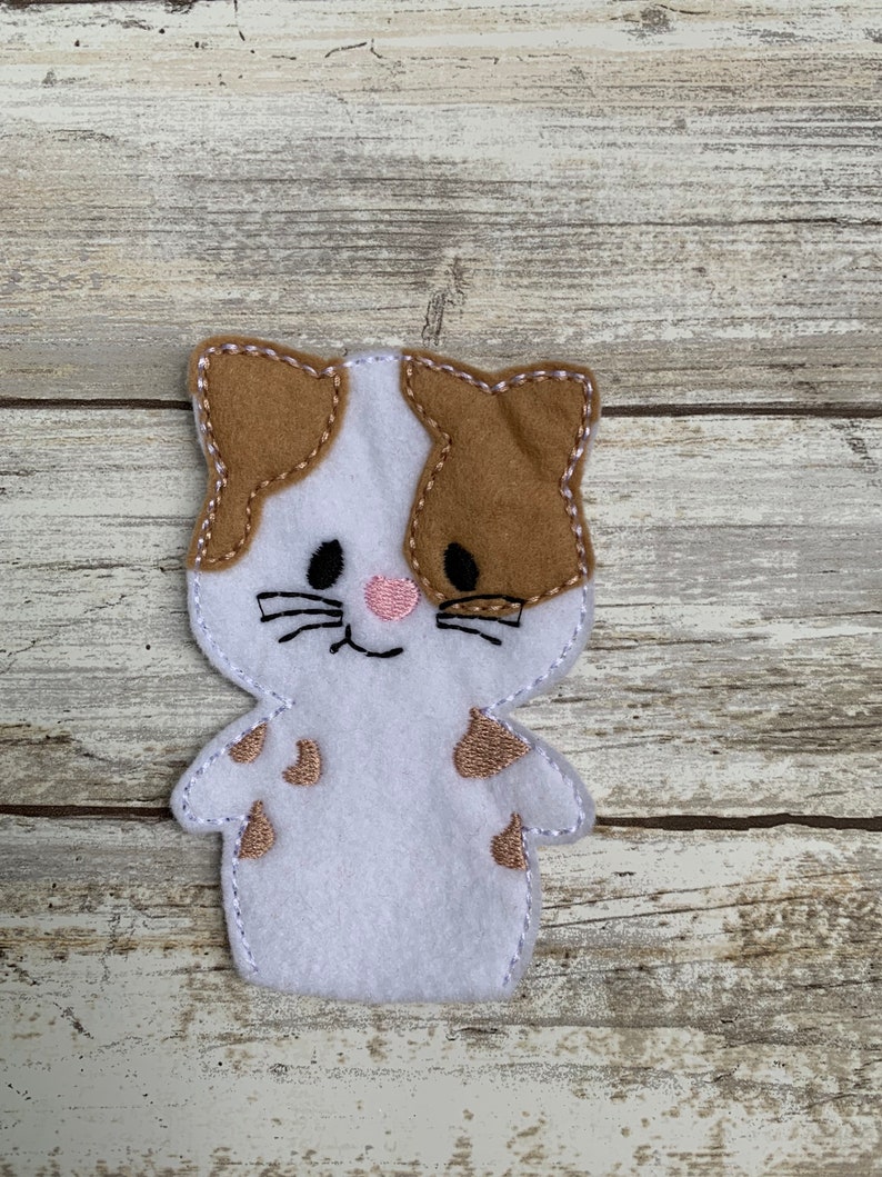 May include: White felt finger puppet with brown felt ears and spots. The puppet has embroidered black eyes, a pink nose, and a smiling mouth.
