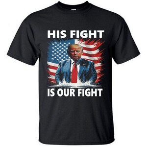May include: Black t-shirt with a graphic of Donald Trump standing in front of an American flag. The text "HIS FIGHT IS OUR FIGHT" is printed on the shirt.