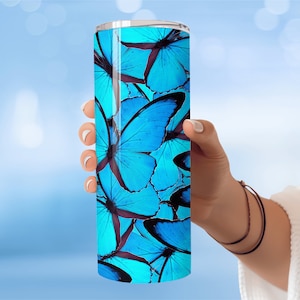 Puede incluir: Un vaso de acero inoxidable con un patrón de mariposa azul. El vaso está diseñado para mantener las bebidas frías o calientes durante horas.